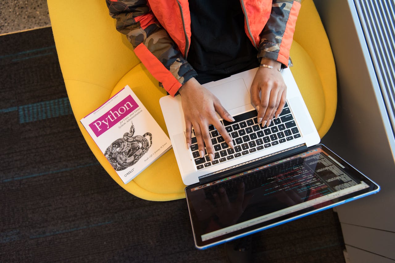 story-02 A developer typing code on a laptop with a Python book beside in an office.